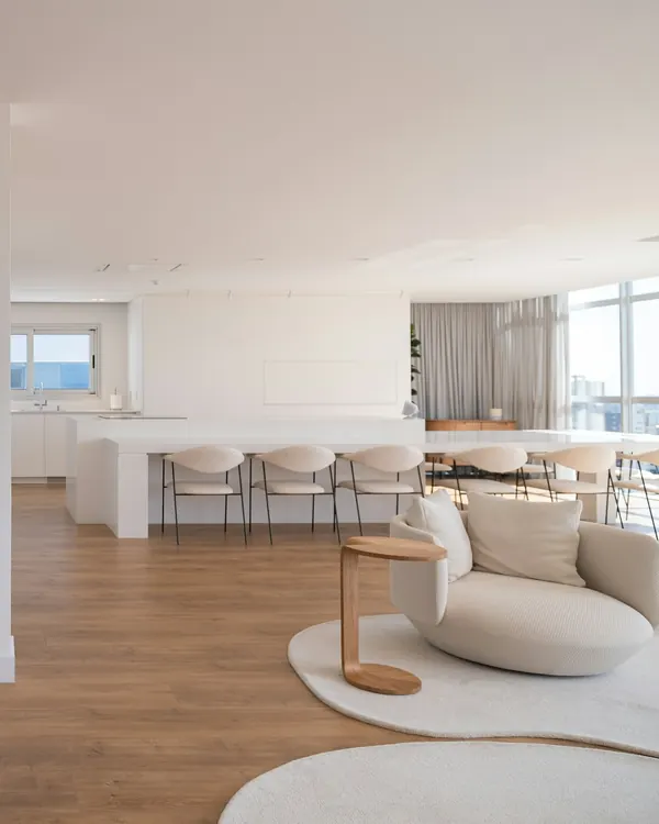 A curved cream armchair in front of an open white kitchen and an oak floor