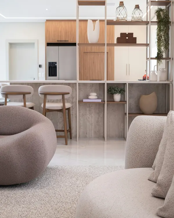 Open oak shelving between the living room and the kitchen, with round bouclé armchairs