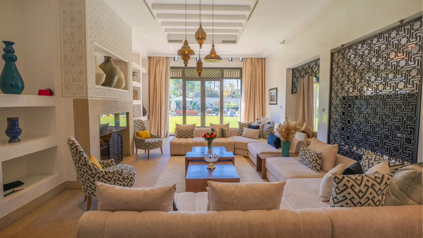 A majlis with beige sofas in a U, brass lanterns, a fretwork screen and glass doors onto the garden