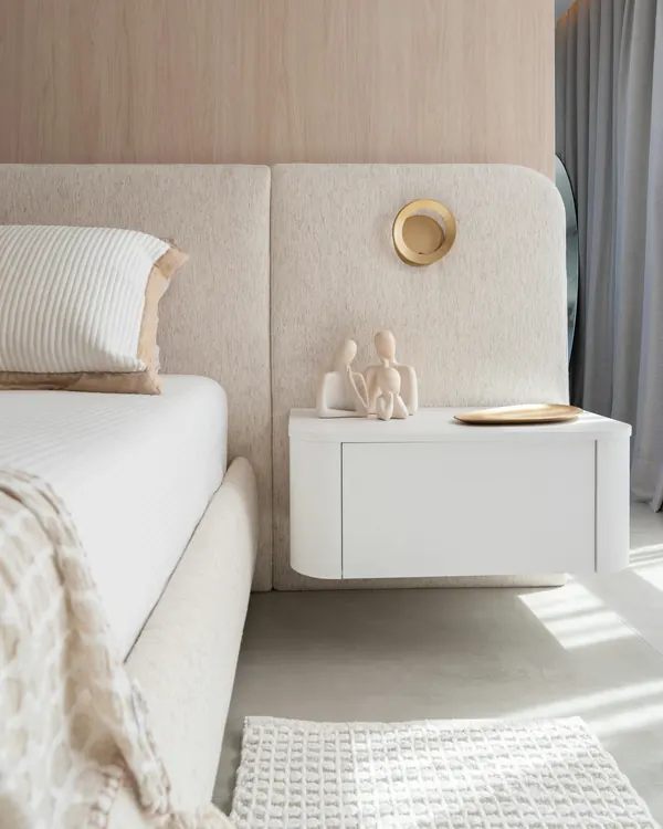 A cream upholstered bed against an oak wall with a floating bedside table