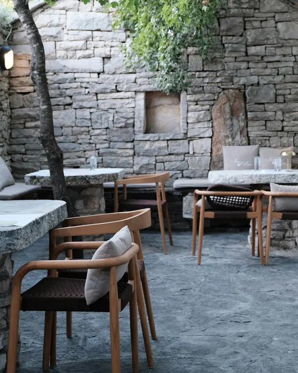 A café courtyard with an old stone wall and timber chairs under a tree