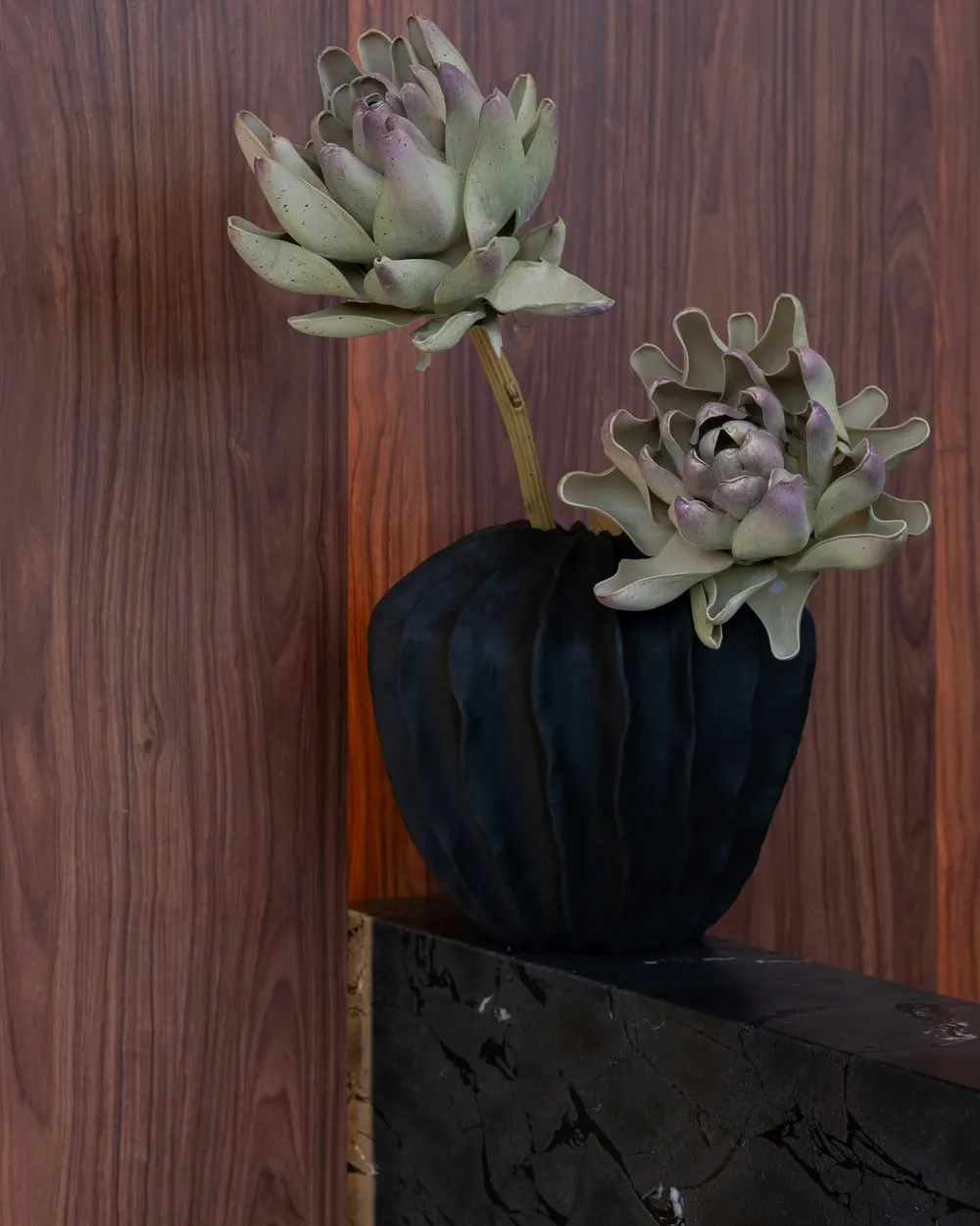 Detail: a dark vase on a stone plinth against walnut
