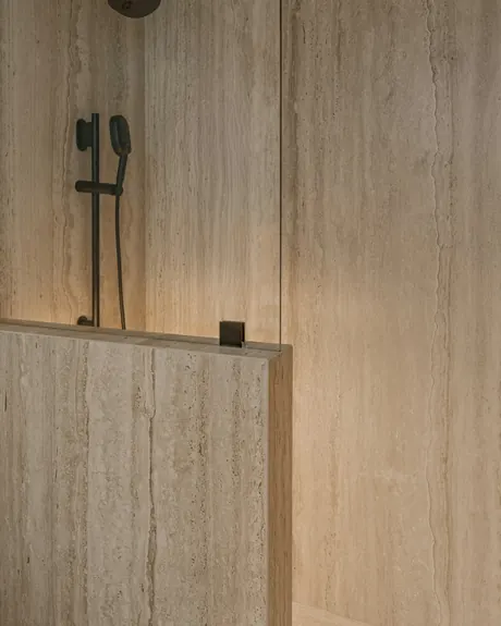 A travertine shower wall with long veins and a black mixer