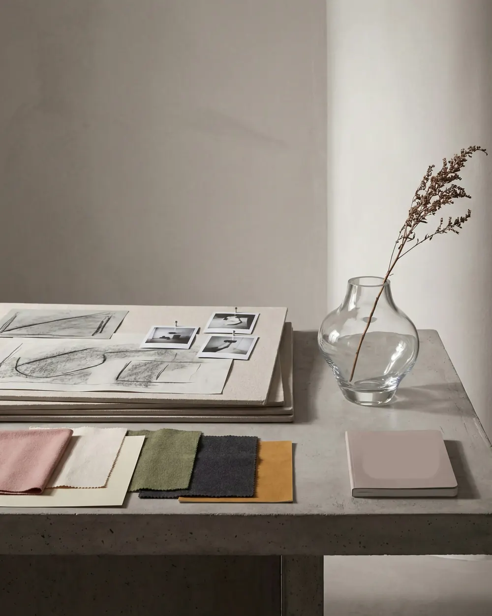 A studio table with charcoal sketches, fabric samples and a glass vase